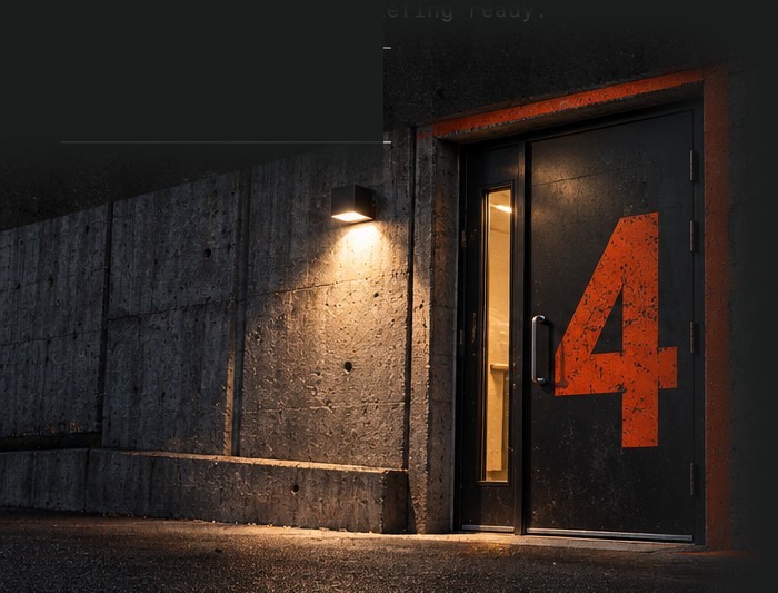 A heavy steel entrance door set in a concrete wall at dusk, with a large orange number 4 painted on it and an orange line along the door frame